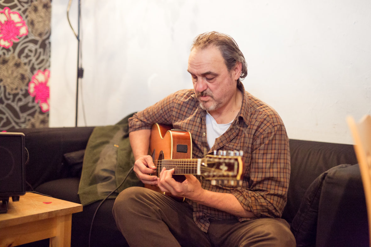 Ein Sozialarbeiter sitzt auf dem Sofa und stimmt seine Gitarre.