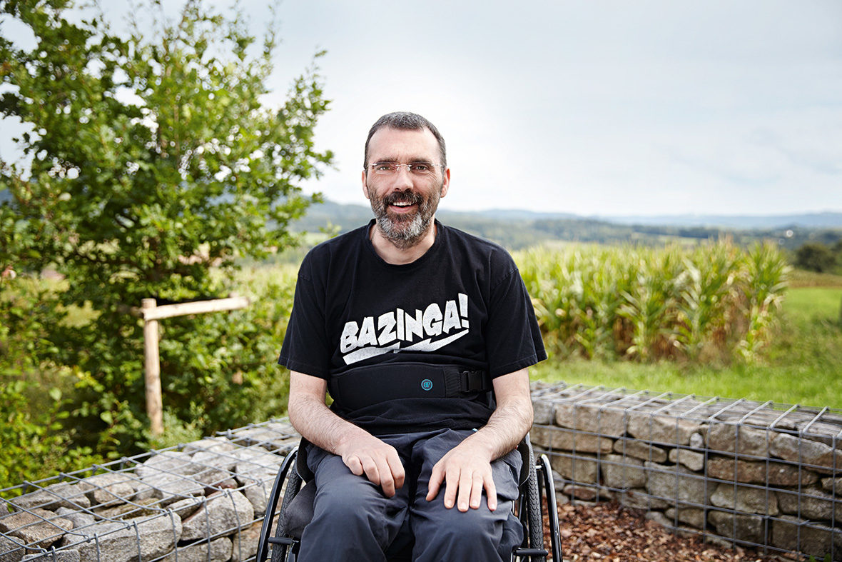 Ein Bewohner sitzt im Rollstuhl auf der Terrasse. Im Hintergrund sieht man die grüne Landschaft.