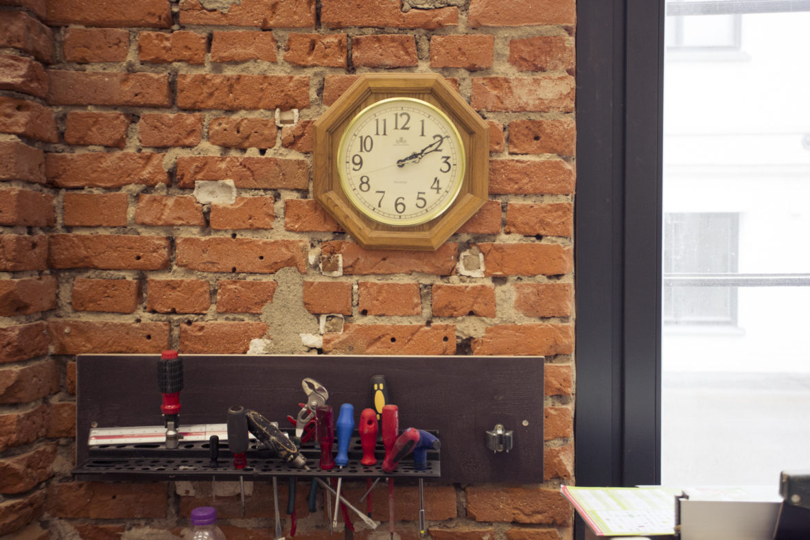 Eine Uhr zeigt zehn nach zwei am Nachmittag an. Darunter befinden sich vor einer unverputzten Backsteinmauer in der Werkstatt allerhand Schraubendreher, etwas chaotisch aufgehängt.