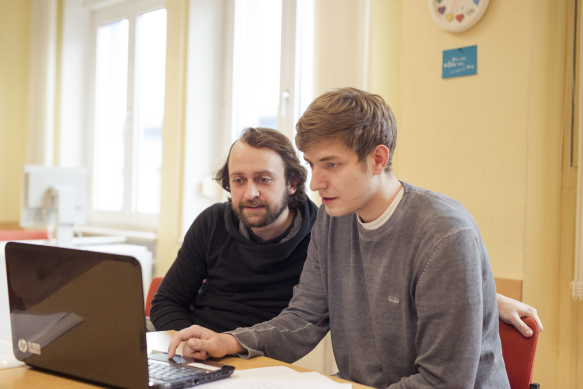 Denis arbeitet am Laptop an seiner Bewerbung zum Fachlageristen. Daniel Reichelt schaut ihm dabei über die Schulter.