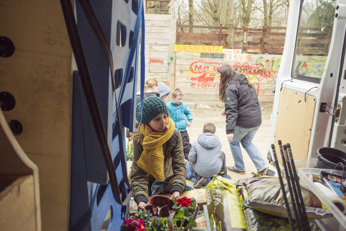 Ein Mädchen steht am Kofferraum des Sportmobils und nimmt einen Blumentopf heraus.