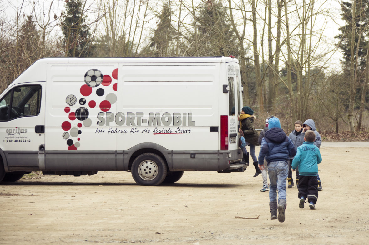 Kinder rennen auf das Sportmobil zu, ein Mädchen steht schon auf dem Trittbrett und schaut hinein.