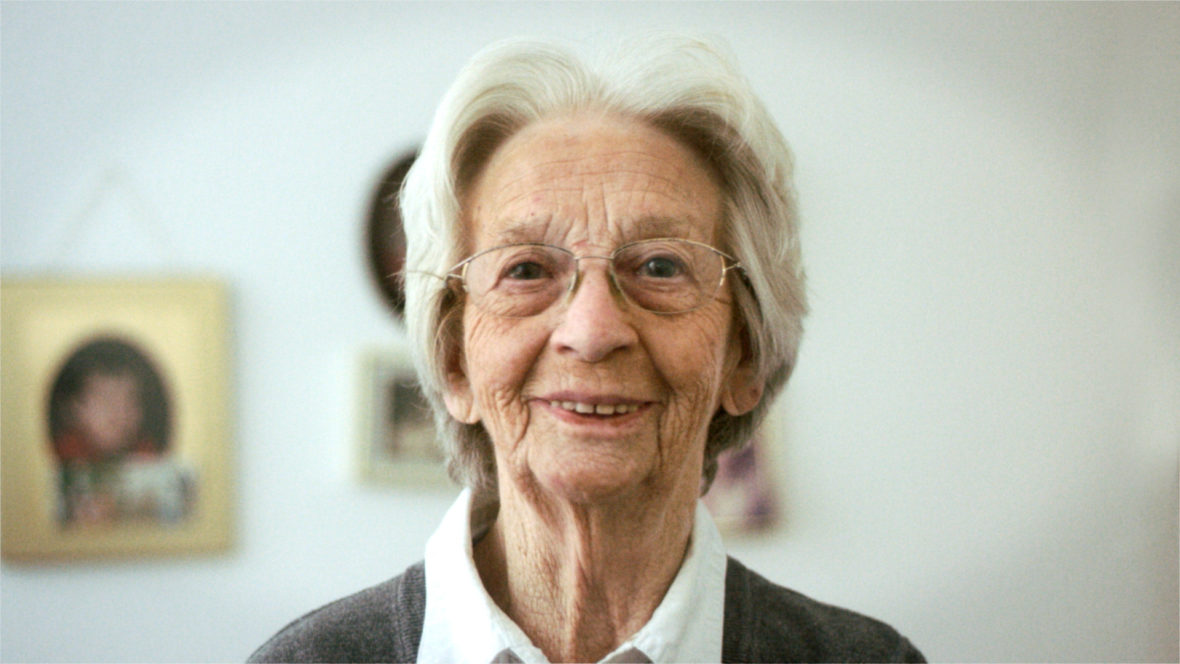 Eine Frau mit Brille und weißem Haar schaut lächelnd in die Kamera