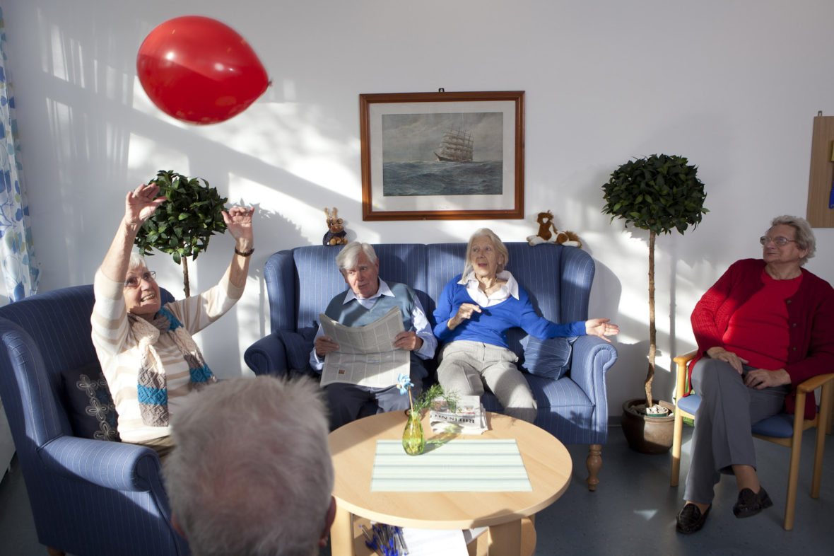 Ältere Bewohner eines Pflegeheims spielen mit einem roten Luftballon.