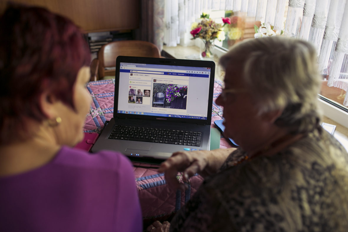 Eine etwas jüngere und eine alte Frau sehen sich eine Seite auf der Plattform Facebook an.