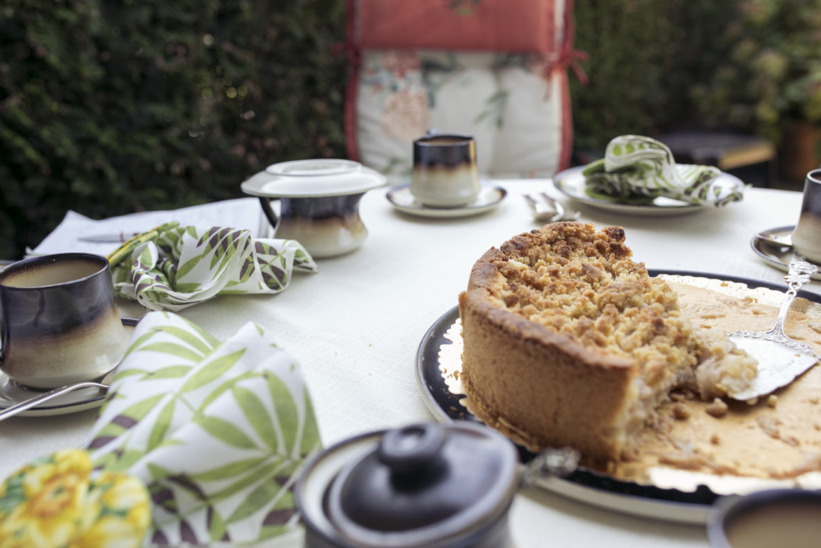 Ein Apfelkuchen steht angeschnitten auf einer schön gedeckten Kaffeetafel.