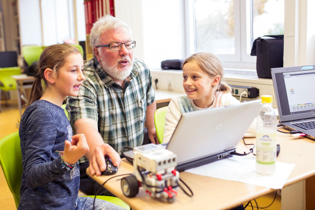Kinder überarbeiten gemeinsam mit einem Senioren ihre Programmierung eines Roboters