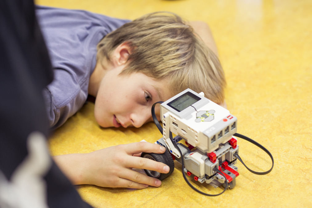 Ein Junge liegt am Boden und betrachtet seinen Roboter