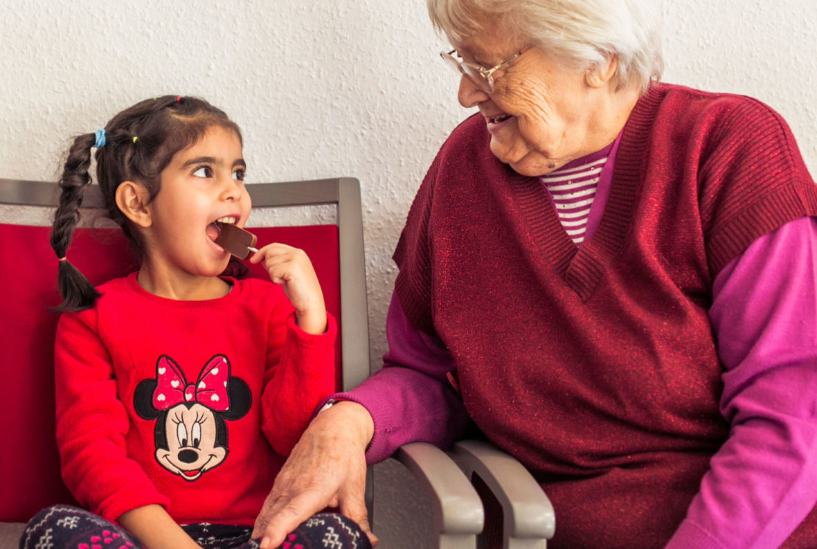 Eine Seniorin schaut erfreut zu, wie ein Mädchen einen Schokololli isst.