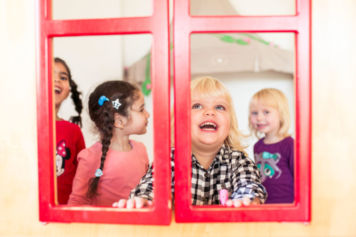 Vier Kinder stehen in einem Spielhäuschen und klappen die Fenster zu und lachen.