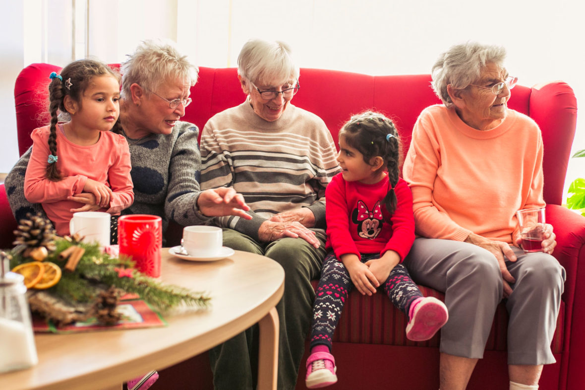 Seniorinnen sitzen mit Kindern auf dem Sofa und unterhalten sich prächtig.