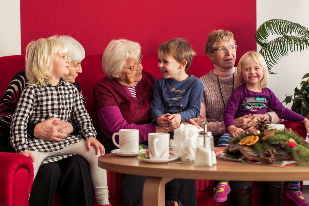 Seniorinnen sitzen mit Kindern auf dem Sofa und Kuscheln