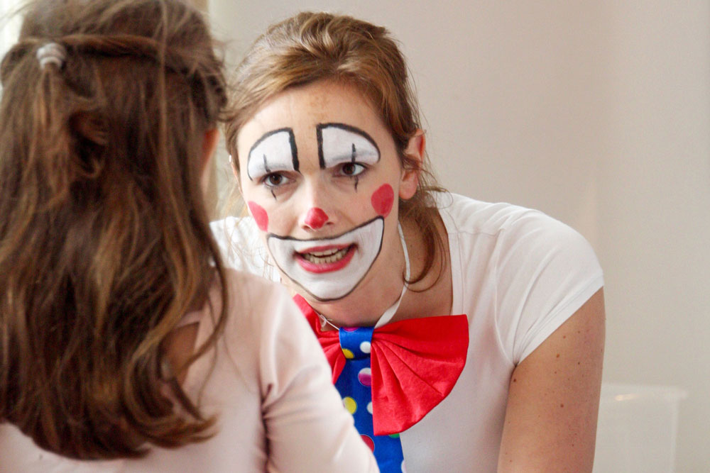 Eine junge Frau ist wie ein Clown geschminkt und spricht mit einem Mädchen.
