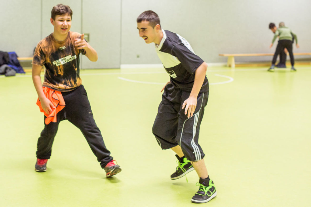 Jungen laufen durch eine Sporthalle und lachen.