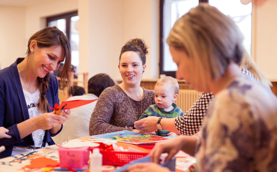 Mehrere Mütter sitzen am Tisch und basteln mit ihren Kindern.