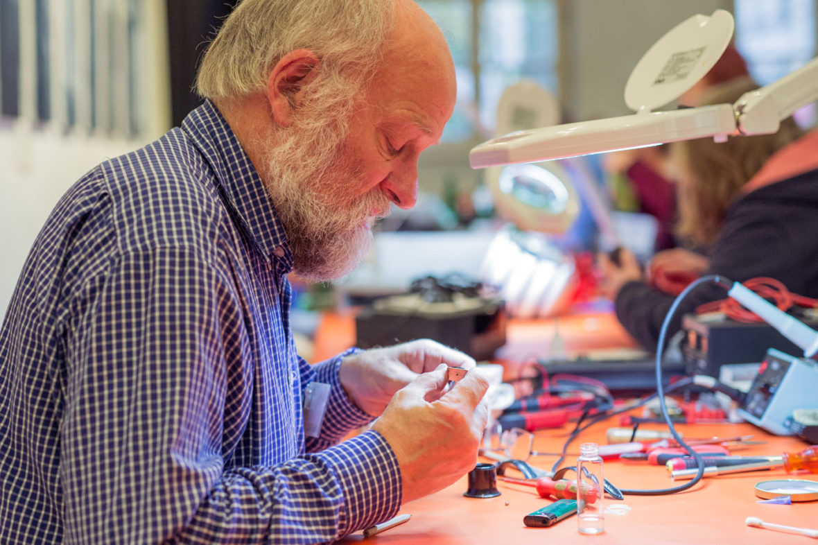 Ein Helfer des Repair-Cafés untersucht ein kleines, elektronsches Ersatzteil.