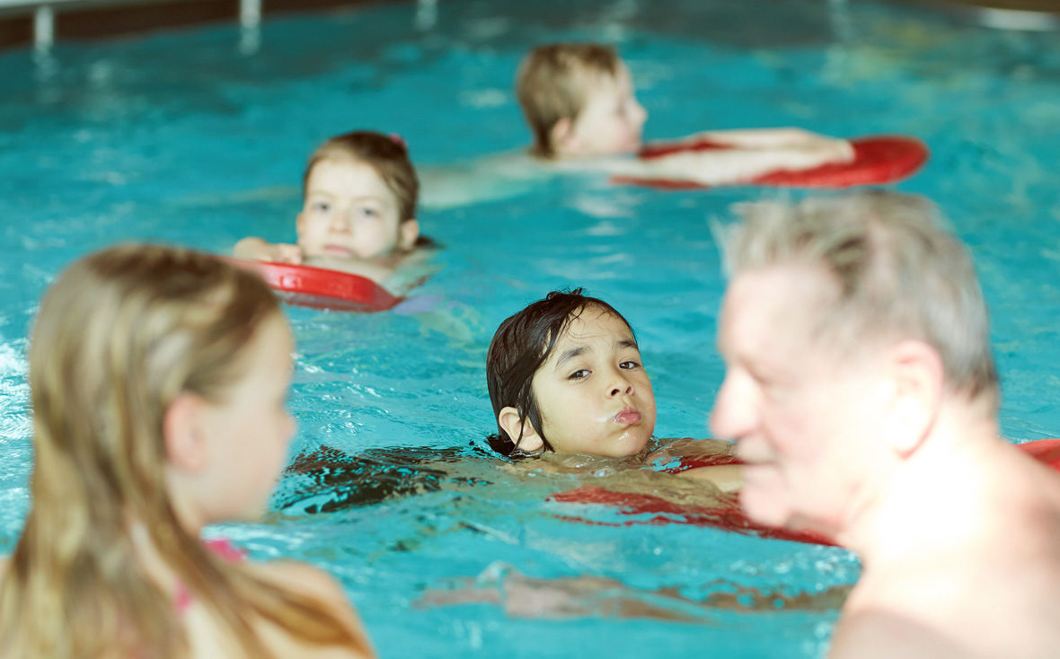 Die Kinder schwimmen mit roten Schwimmbrettern