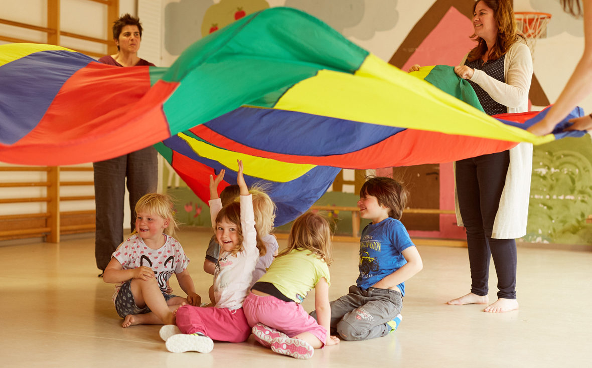 Gruppe Kinder sitzt unter einem bunten Tuch