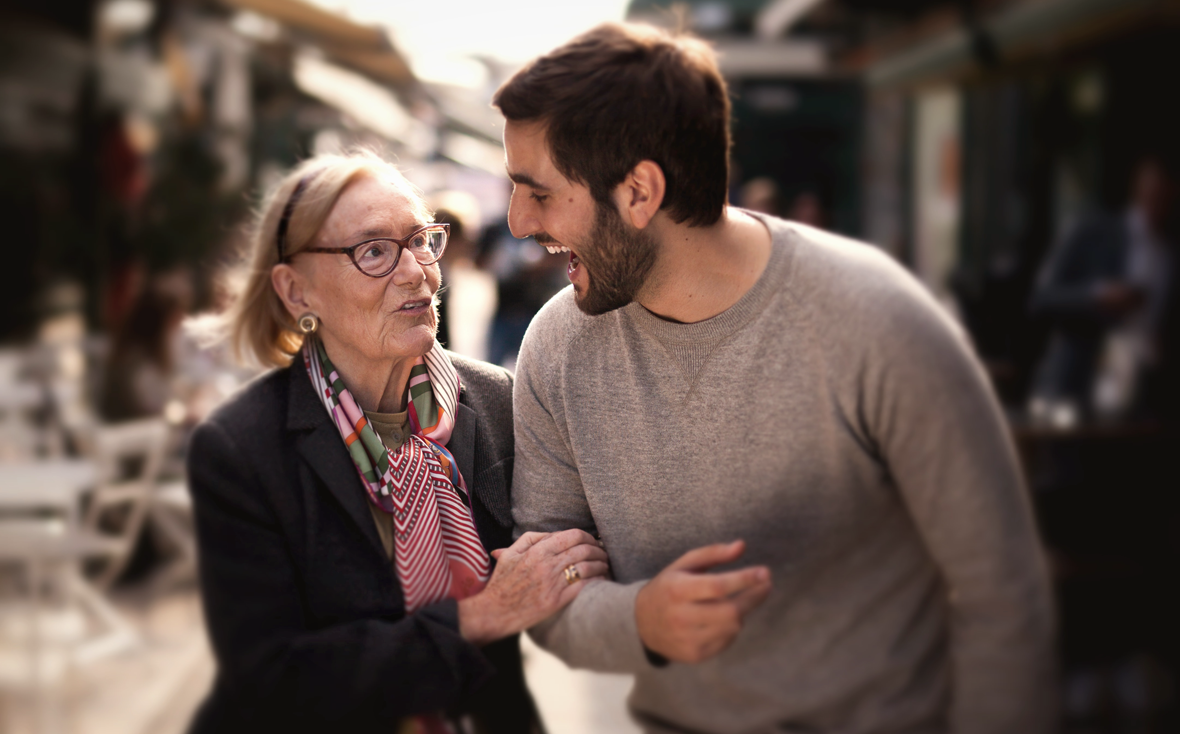 Eine ältere Dame geht Arm in Arm mit einem jungen Mann spazieren