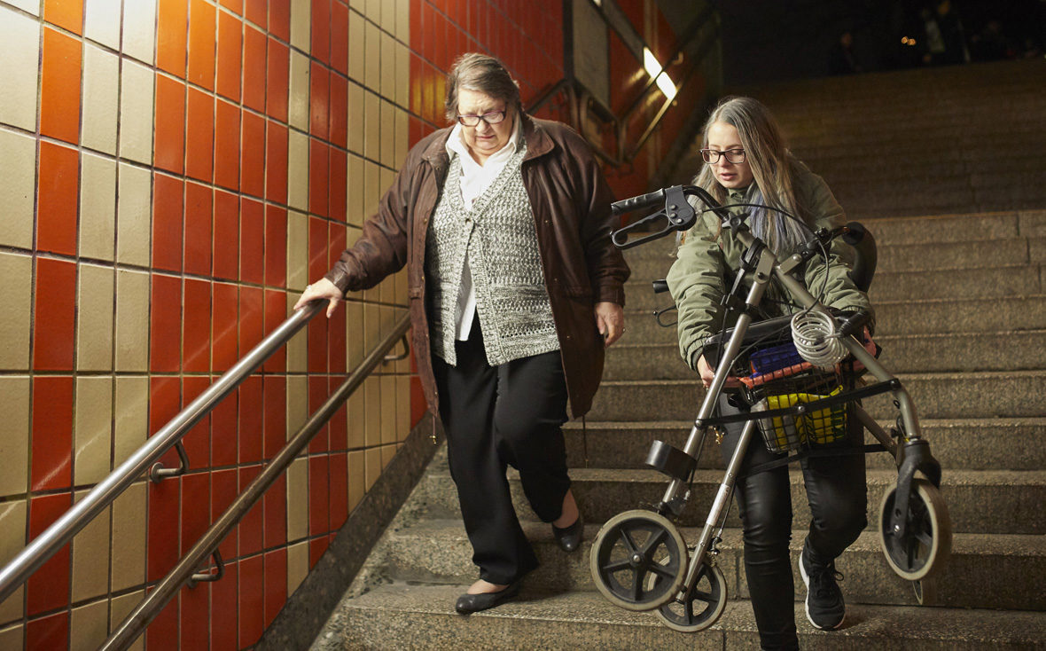 Kulturisten Hoch2: Julia trägt Frau Rieper den Rollator die Treppe runter.