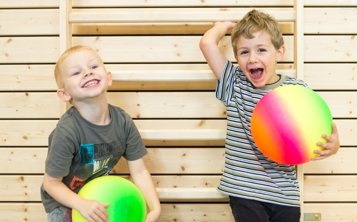 Zwei Jungen spielen in der Turnhalle mit bunten Bällen.