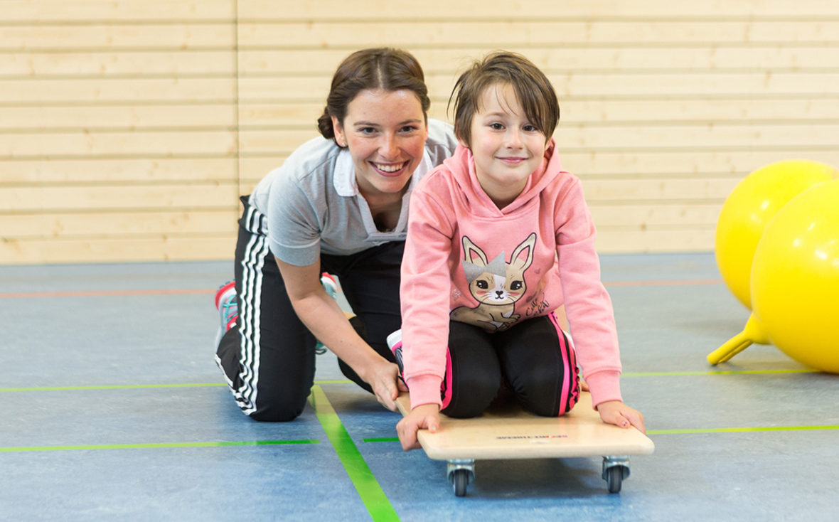 Physiotherapeutin Marleen Reuter mit einem Kind auf einem Rollbrett.