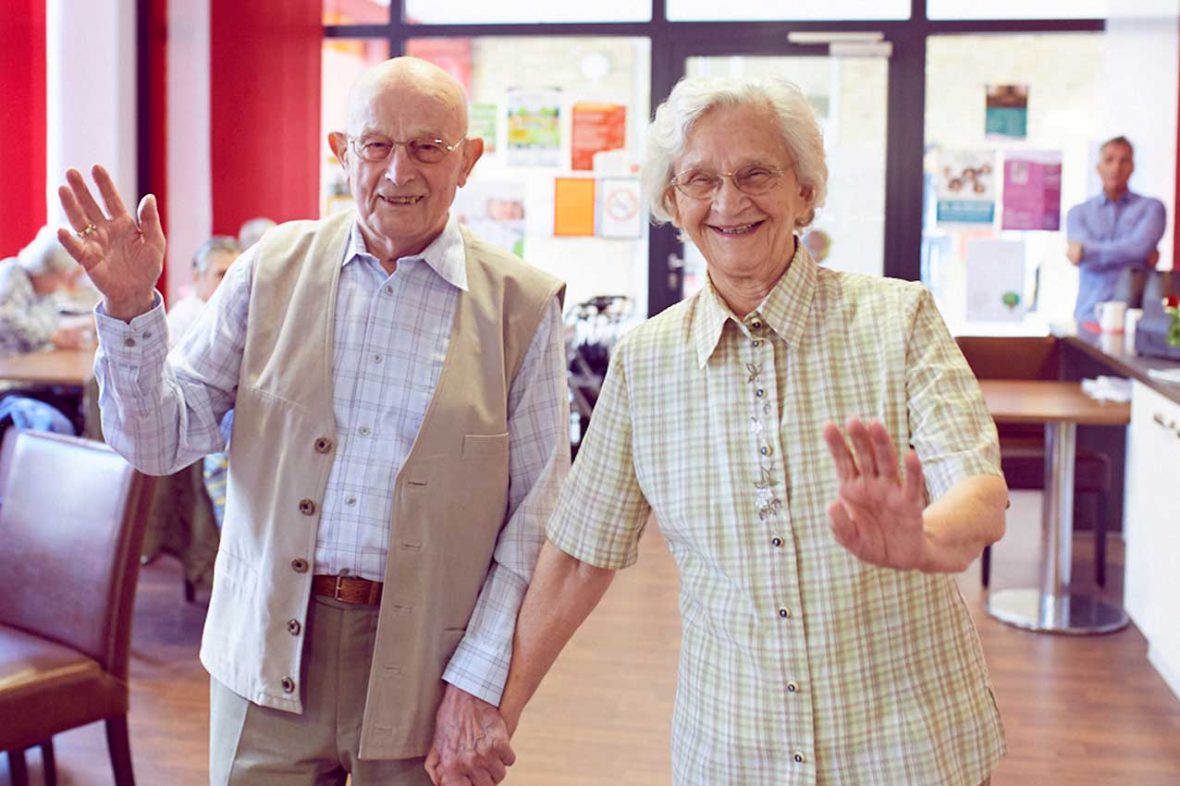 Zwei Besucher des Tanztees winken lachend und halten sich an der Hand.
