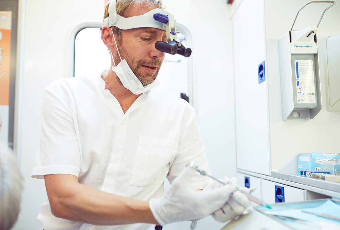 Dr. Uphoff bereitet im Zahnmobil Hamburg eine Salbe vor, die er seinem Patienten auf das Zahnfleisch aufrägt.