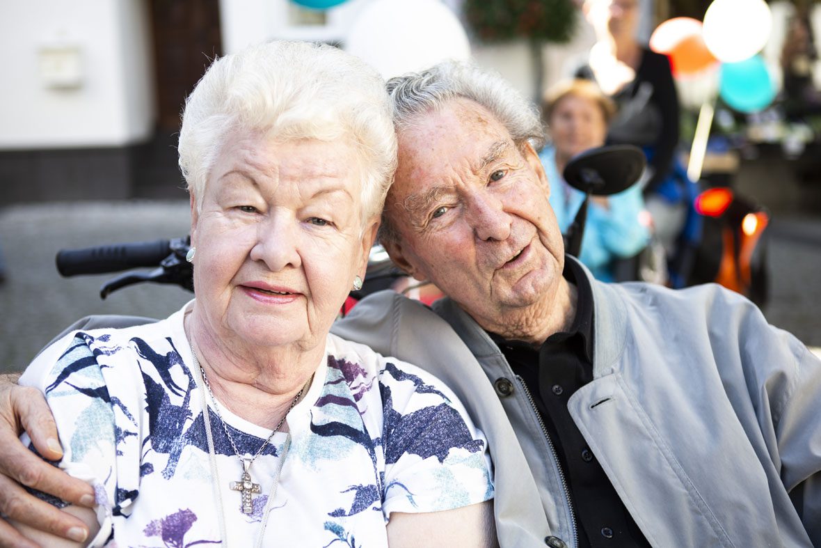 Ein älterer Herr und eine ältere Dame schauen fröhlich in die Kamera. Sie sitzen nebeneinander in der Rikscha.
