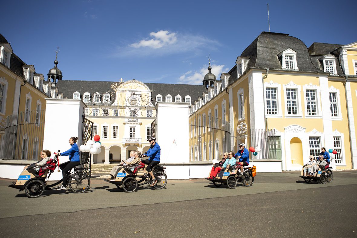 Vier Fahrradrikschas mit Faherer*innen und Passagieren fahren am Schloss Oranienstein in Diez entlang.