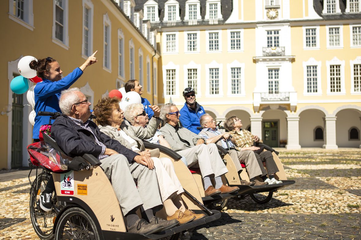 Caroline und die anderen Ehrenamtlichen schauen gemeinsam mit den Senior*innen das Schloss aus den Rikschas aus an.