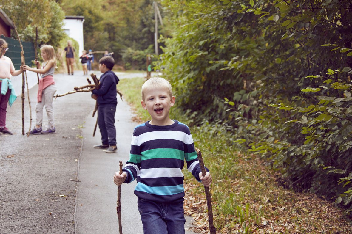 Ein Junge im gestreiften Pulli läuft mit zwei Stöcken in der Hand einen Weg entlang.