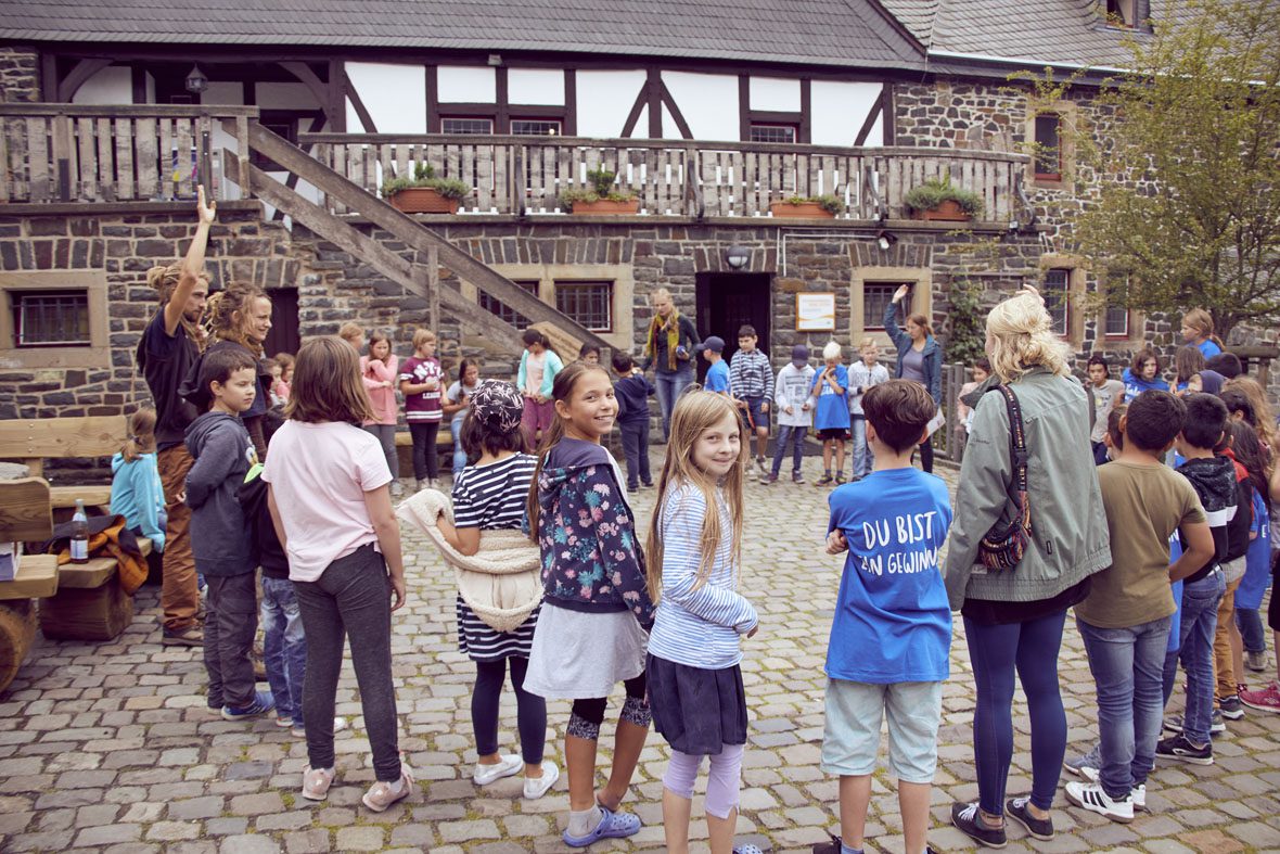 Die Kinder stehen im Kreis, im Hintergrund ist ein Teil der Burg Altena zu sehen.