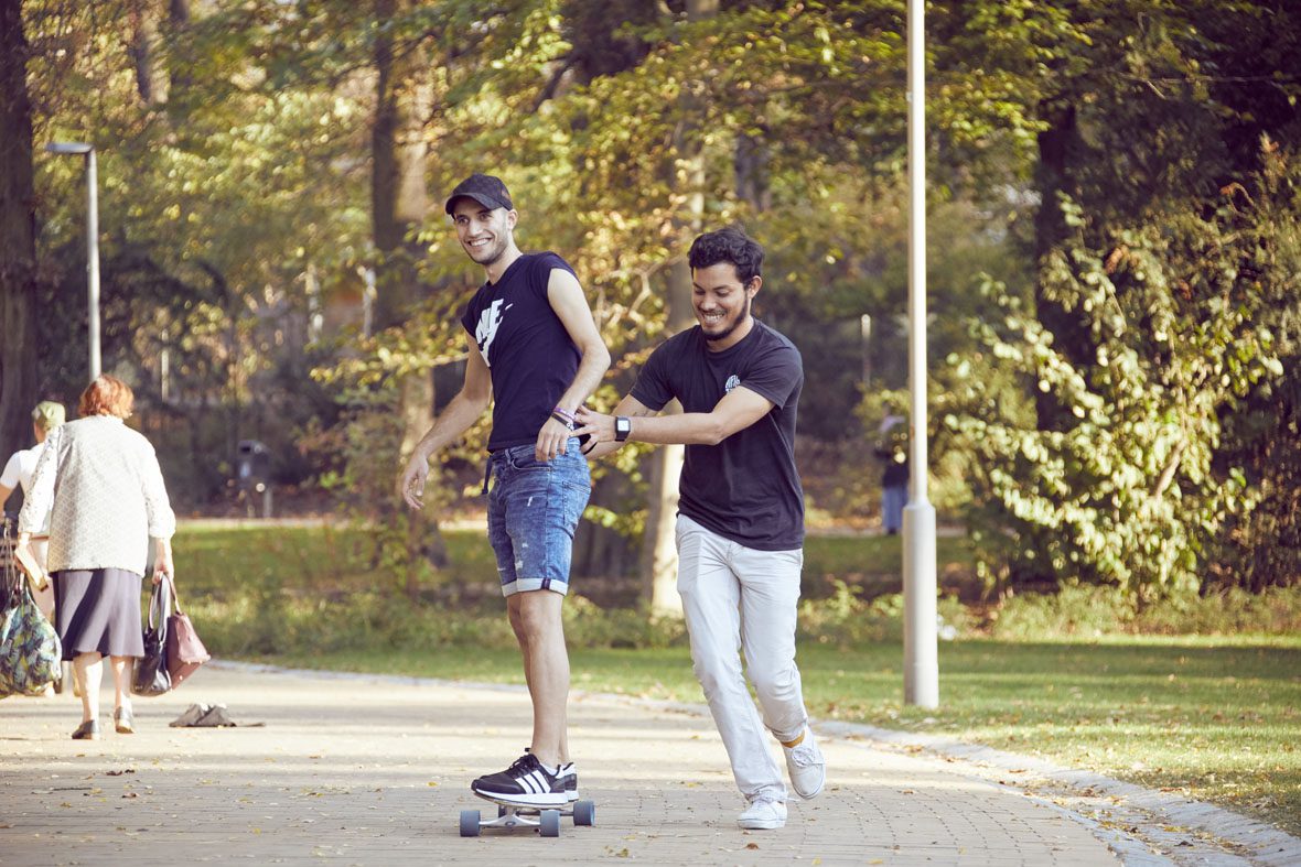 Salam versucht sich am Longboardfahren, Eduardo stützt ihn dabei und läuft neben dem Board her.