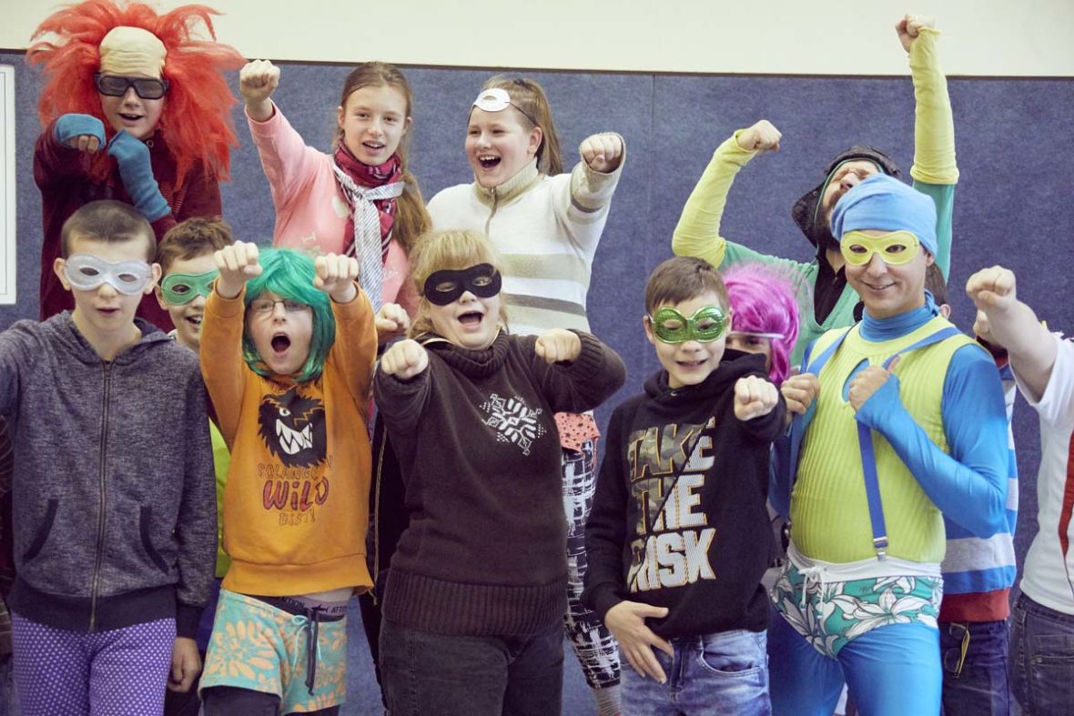 Die Kinder stehen in einer Gruppe, sie sind verkleidet und recken eine Faust in die Höhe.