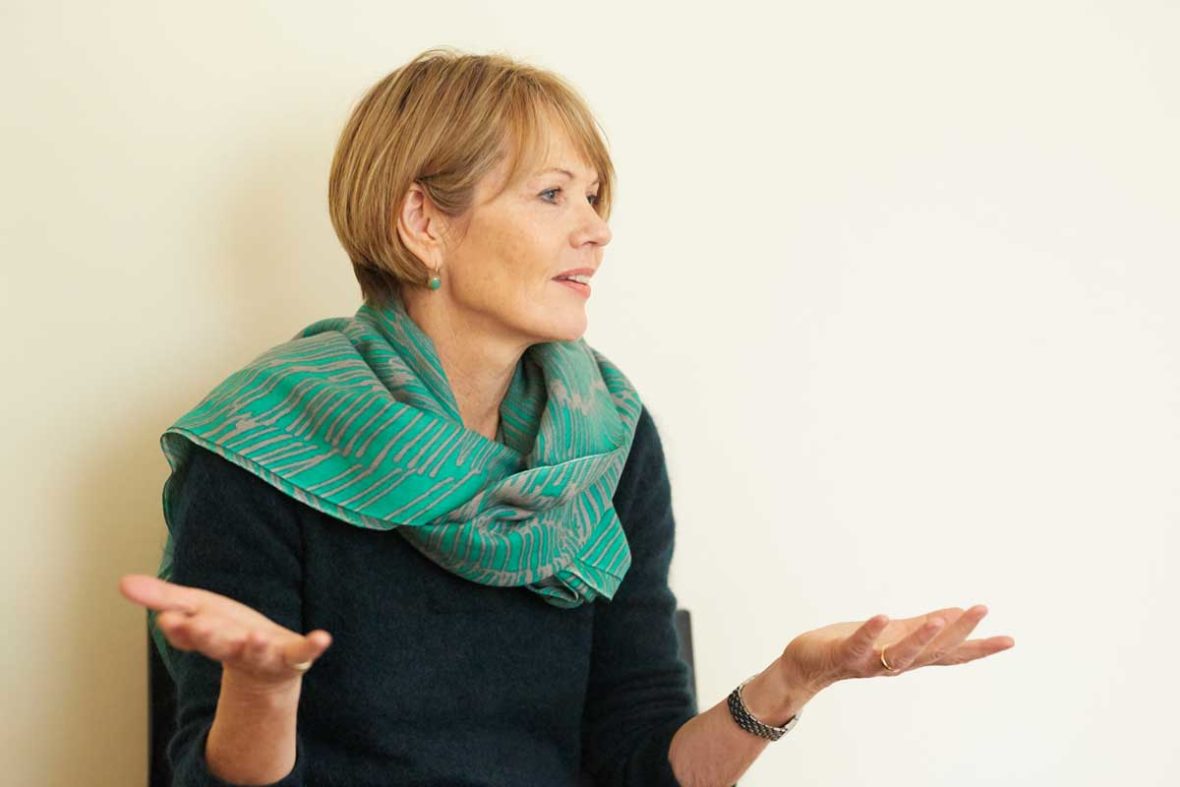 Hannah Friedl sitz vor der Wand und erzählt, dabei gestikuliert sie mit den Händen.