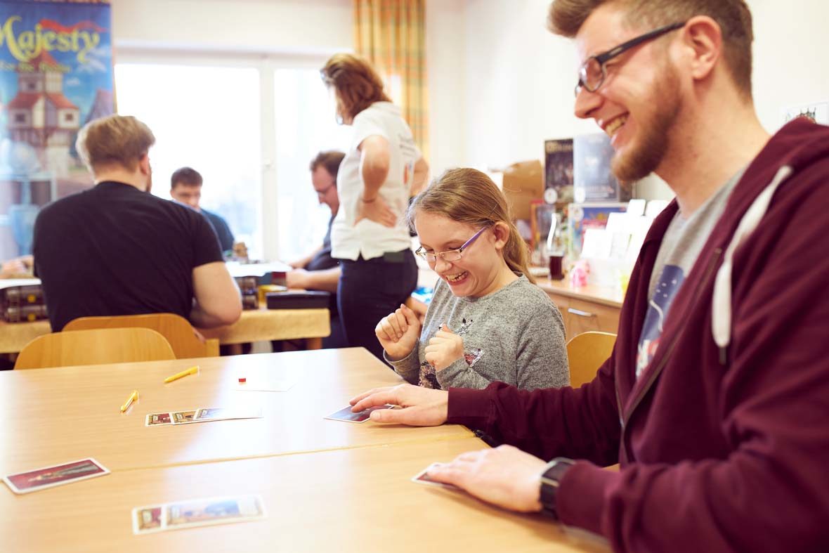 Ein junges Mädchen schaut aufgeregt auf seine Spielkarte, die ihm gerade hingeschoben wird. Es hält die Hände zu Fäusten geballt aufgeregt for der Brust.