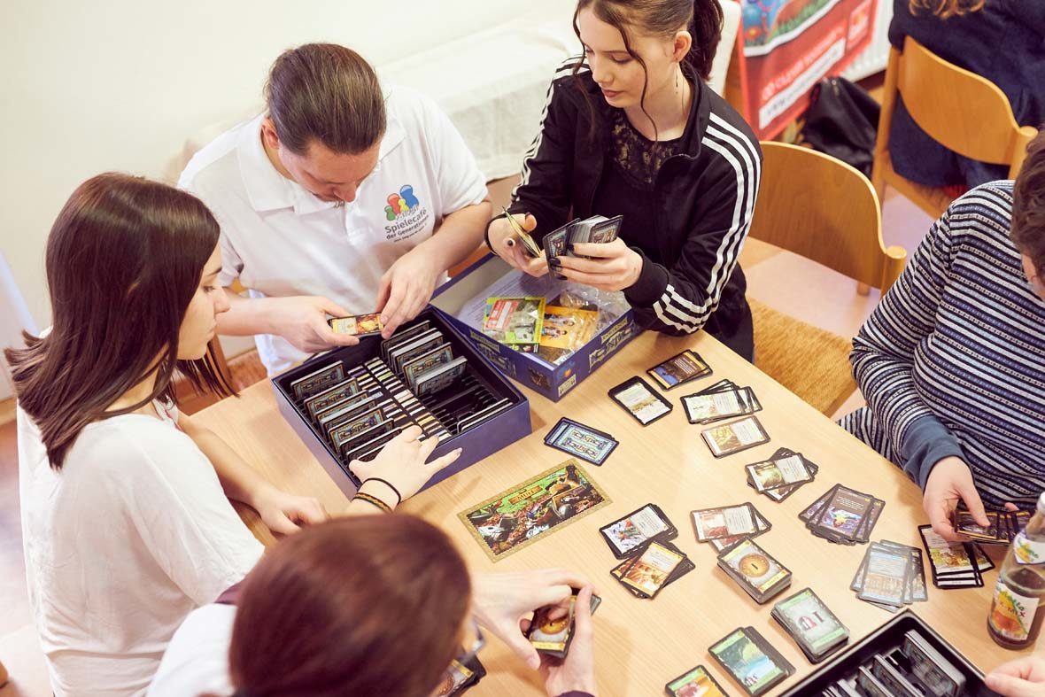 Eine Gruppe junger Menschen sitzt um einen Tisch, auf dem Tisch liegen Spielkarten.