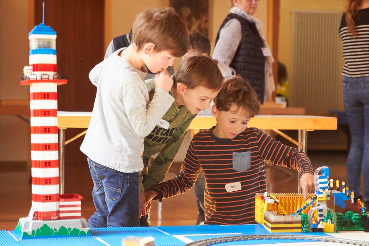Drei Jungs schauen sich ein LEGO-Gebäude an. Neben ihnen steht außerdem ein LEGO-Leuchtturm.