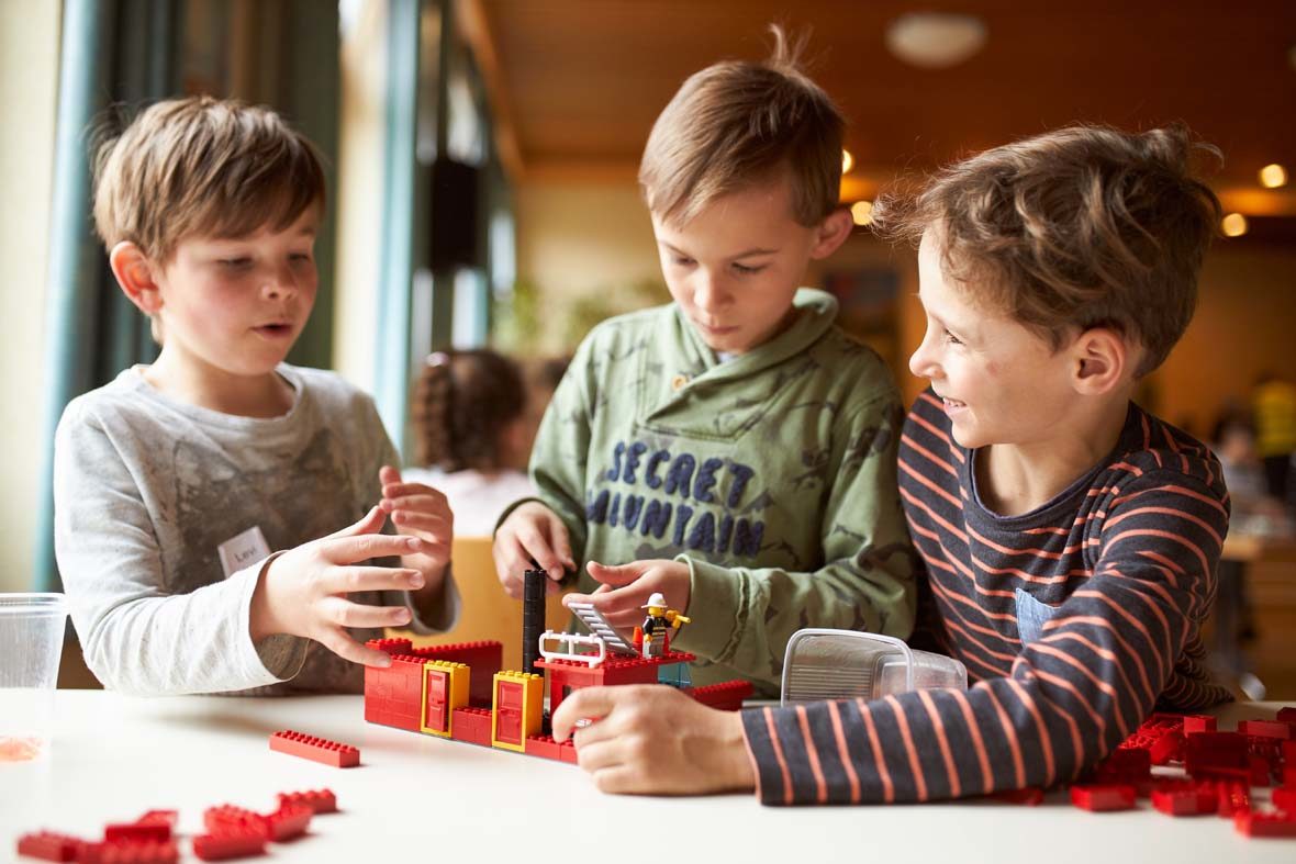 Drei Jungs bauen mit LEGO-Steinen ein Gebäude.