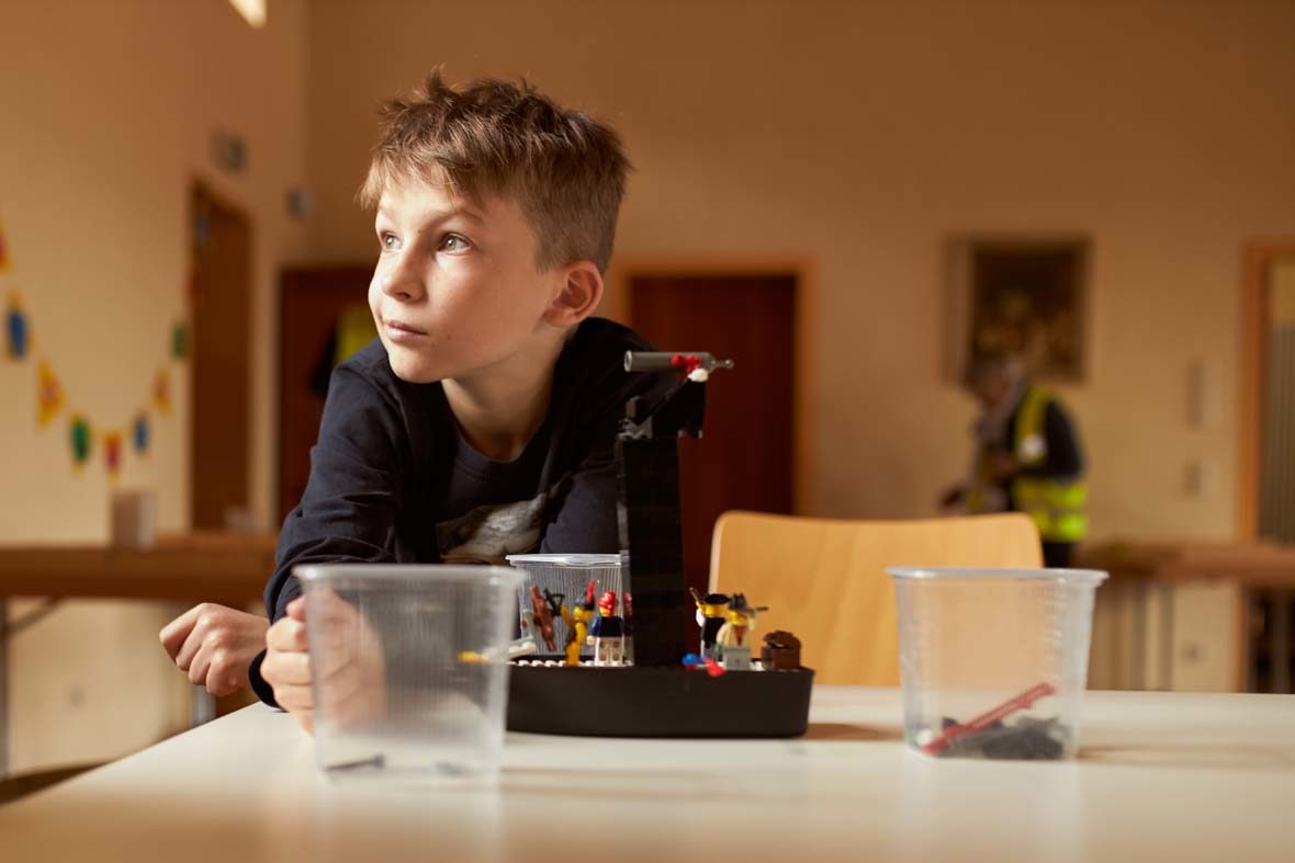 Ein Junge sitzt vor einer LEGO-Konstruktion und schaut in eine andere Richtung.