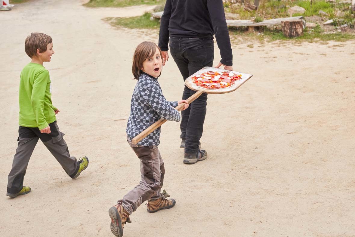 Kleiner Junge trägt Pizza auf einem Holzschieber.
