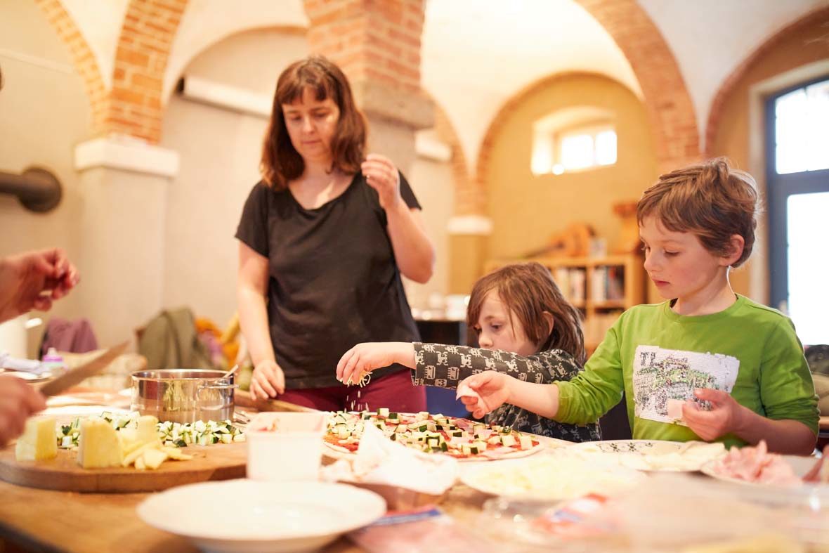 Eine Frau und zwei Kinder bestreuen Pizzateig mit Käse.