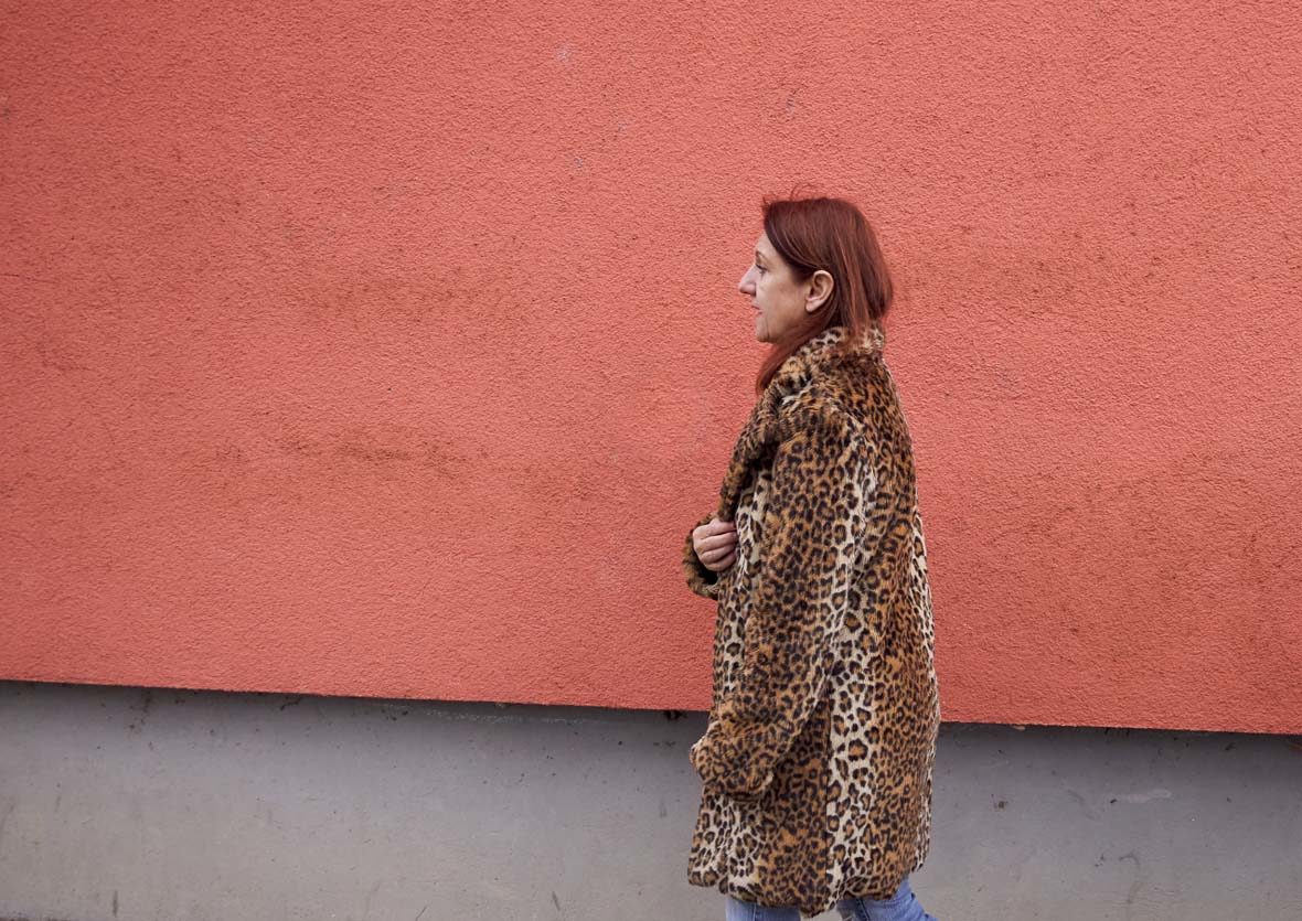 Frau im Kunstfellmantel läuft an Hauswand vorbei.