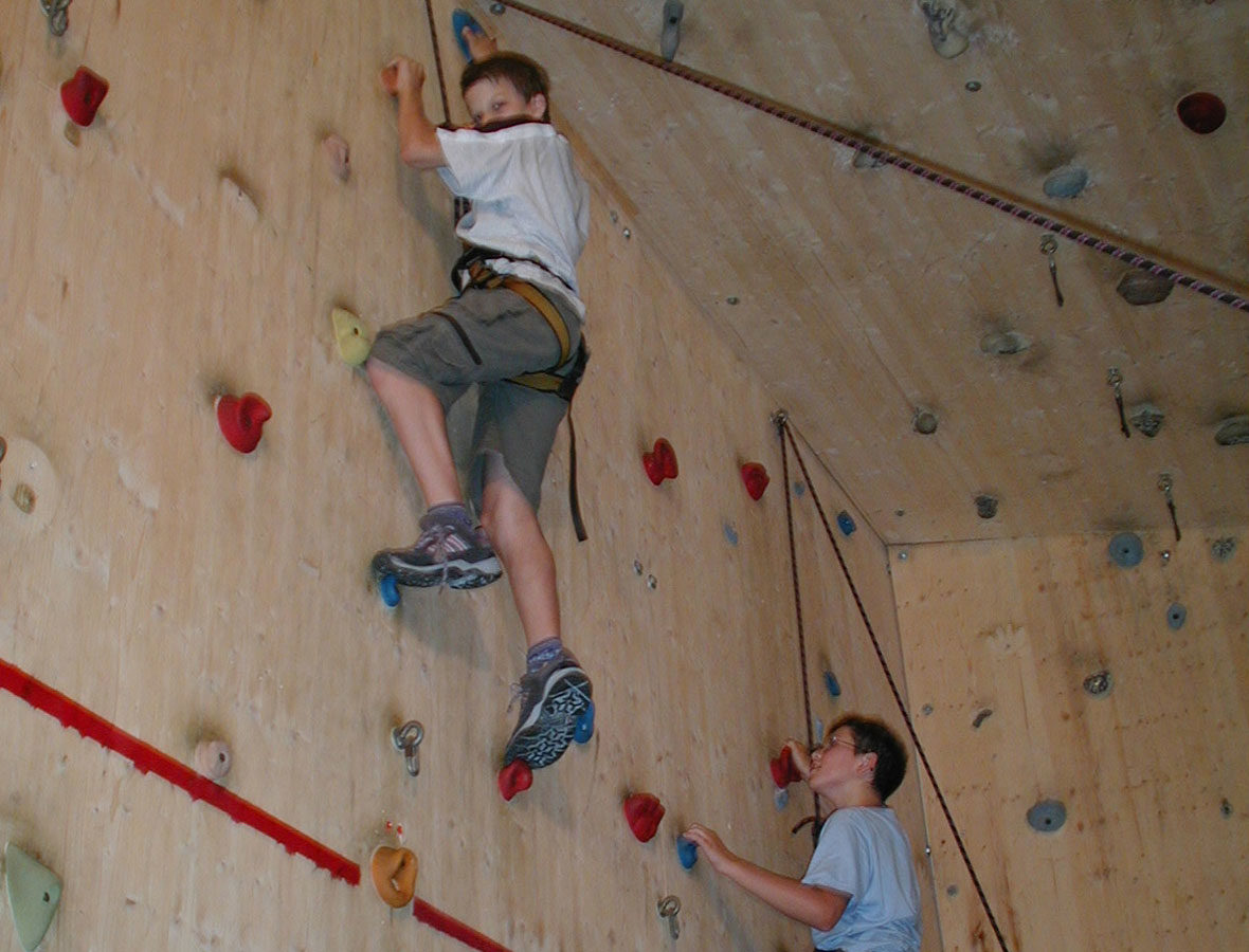 Foto: Ein Junge klettert in der Kletterhalle und ist mit einem Seil gesichert.