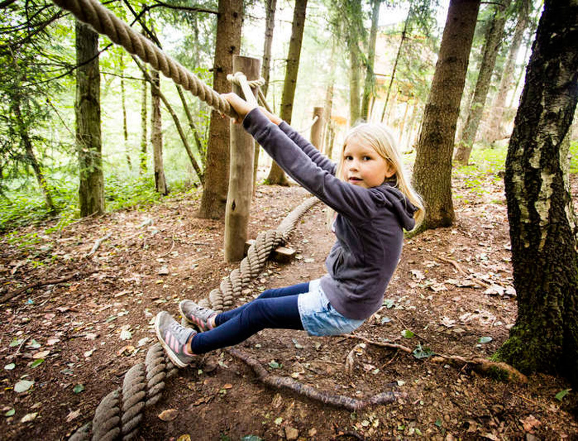 Foto: Ein Mädchen klettert im Wald an einem Seil.