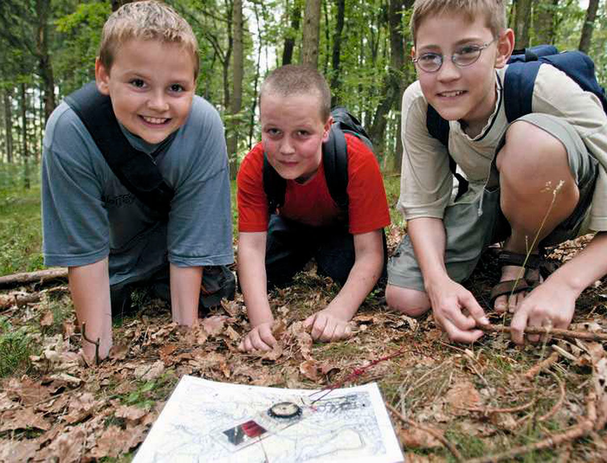 Foto: Drei Jungen sitzen auf dem Waldboden, vor ihnen eine Karte und ein Kompass.