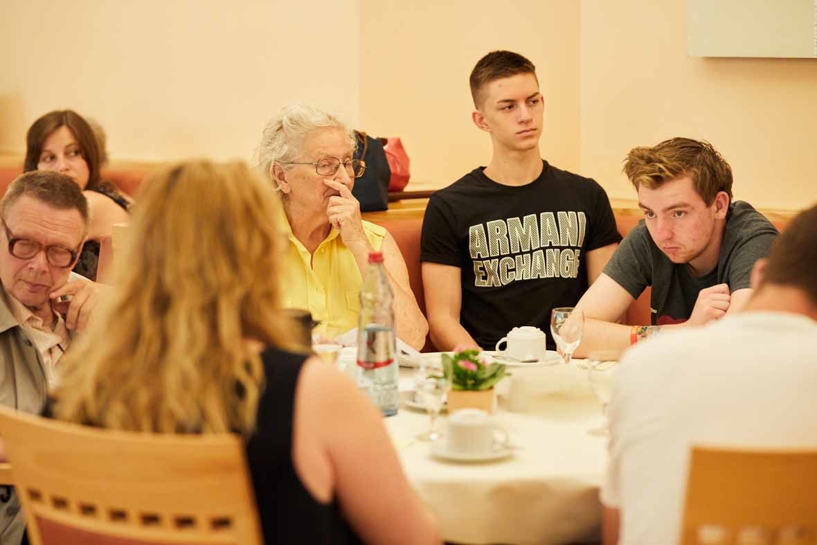 Foto: Junge und ältere Menschen sitzen an einem Tisch, hören zu und schauen betroffen