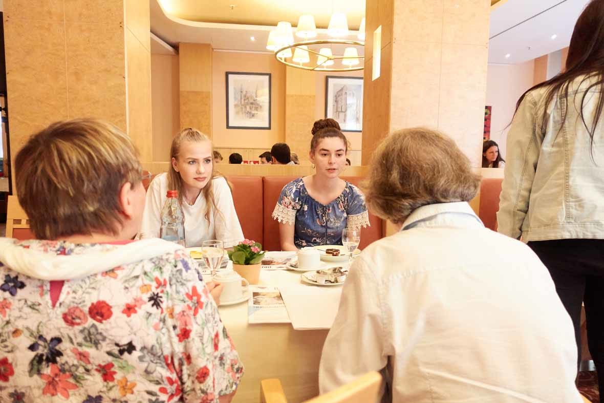 Foto: Zwei junge Frauen unterhalten sich mit zwei älteren Frauen am Tisch