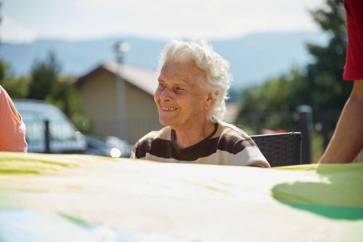 Foto: Eine alte Frau sitzt auf einem Stuhl und lächelt, vor ihr ist ein Schwungtuch